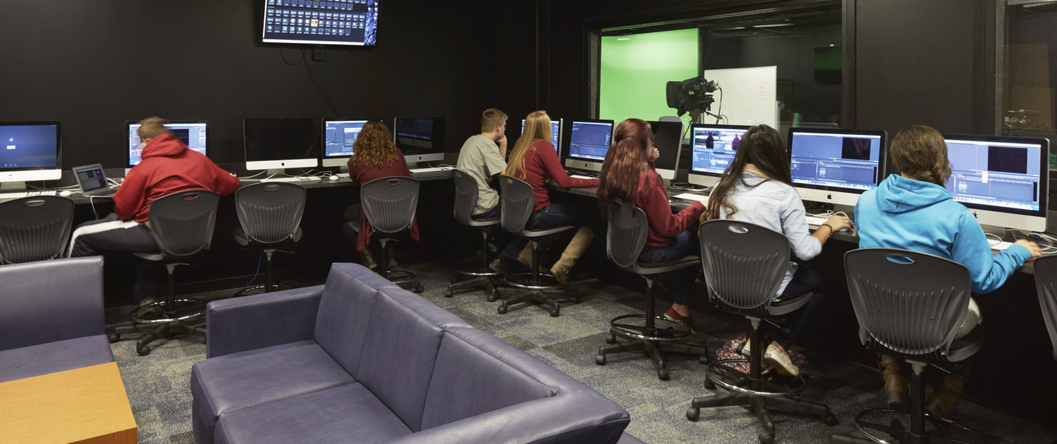 Computers with video editing equipment line 2 walls facing away from couches. Window, right looks to greenscreen and lighting