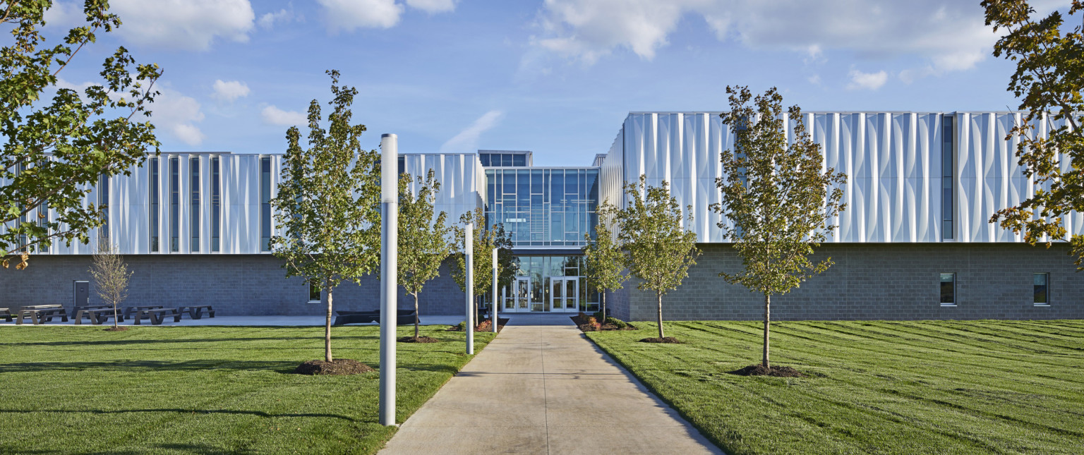 Front view of building looking down a treelined path to the front entrance with 2 sets of glass double doors