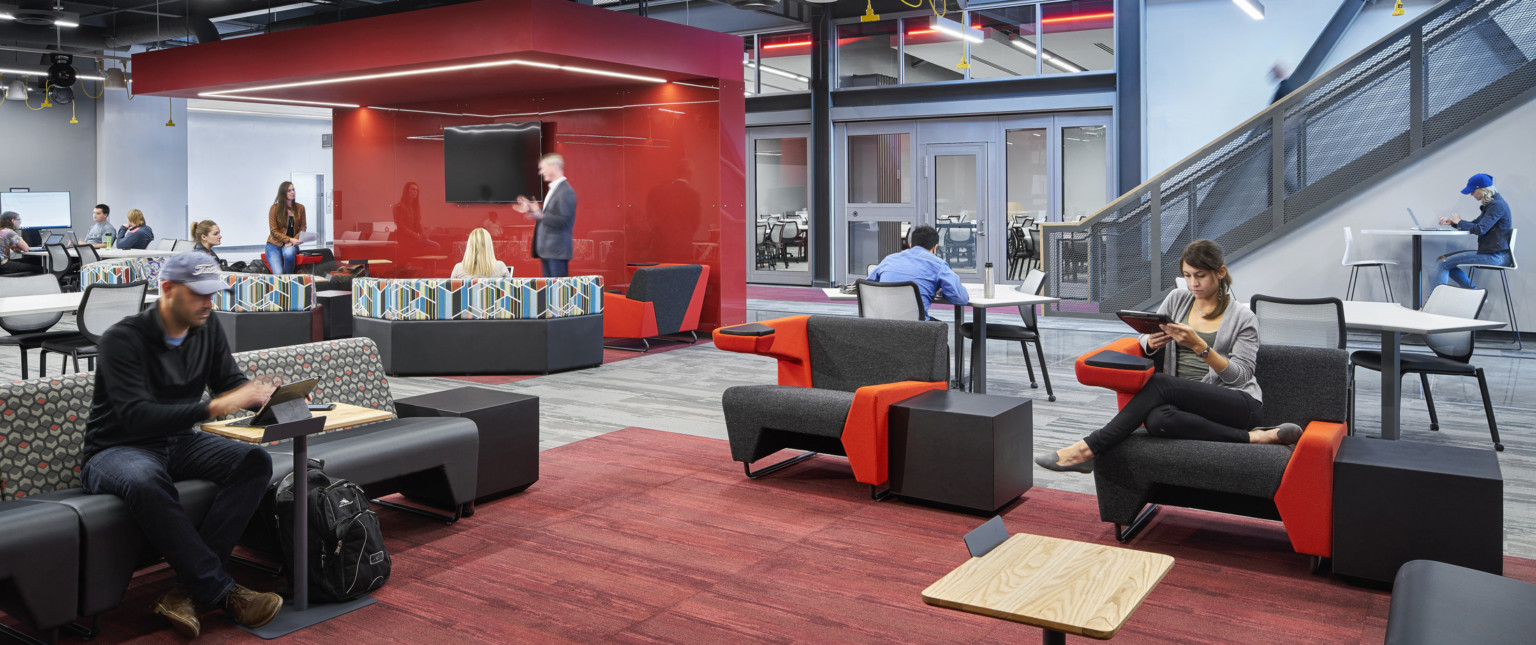 Carpeted seating area. Left, a red partition and illuminated canopy separates a section. A staircase with grey rail is right