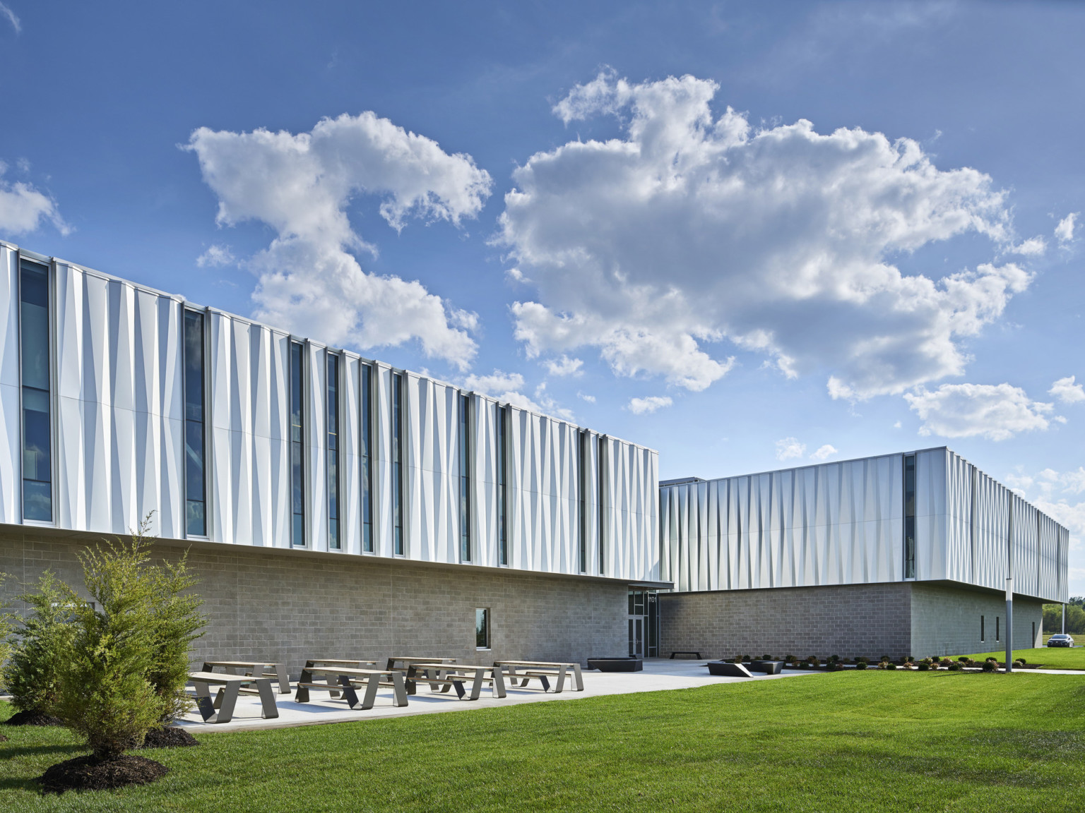 Side view of building shows patio to left of entrance with picnic tables. Upper half of building has recessed thin windows