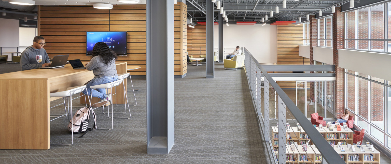 Seating areas on 2nd floor with wood panel accent walls overlooking 1st floor library. Double height windows on right wall