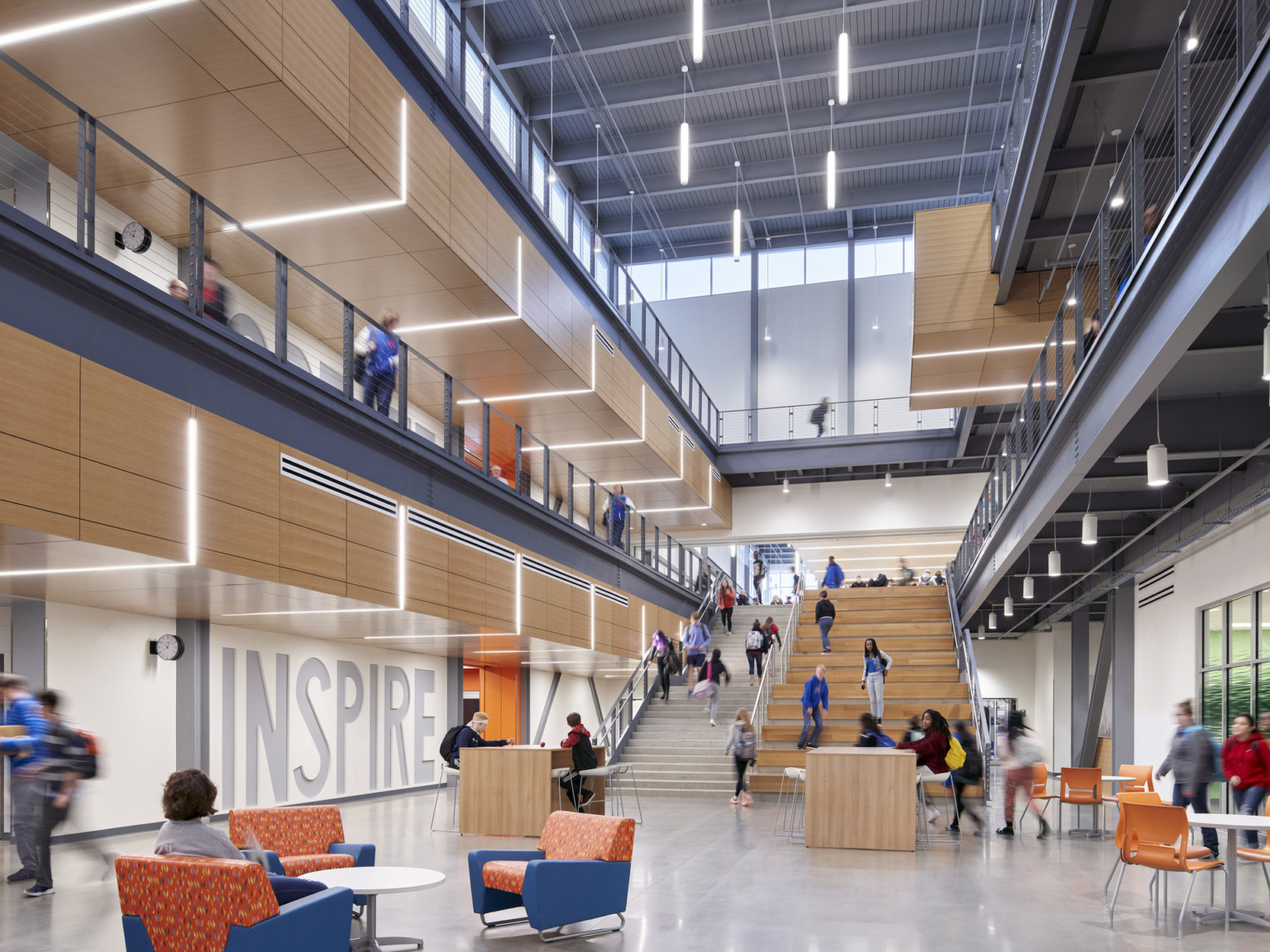 Triple height atrium with seating at base of stairwell with stepped benches. Walkways at each level. Inspire written on left