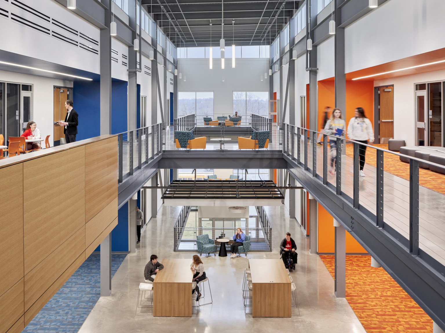 End of 3rd floor walkway looking down with views to 1st floor. Seating on each level. Blue accents left, orange right.