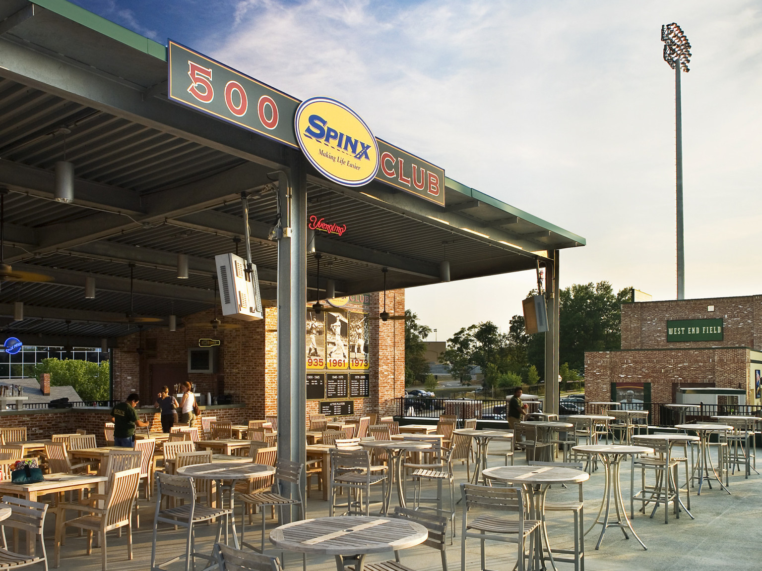 Partially covered outdoor dining area with green awning extending from concession stand with Spinx 500 Club sign