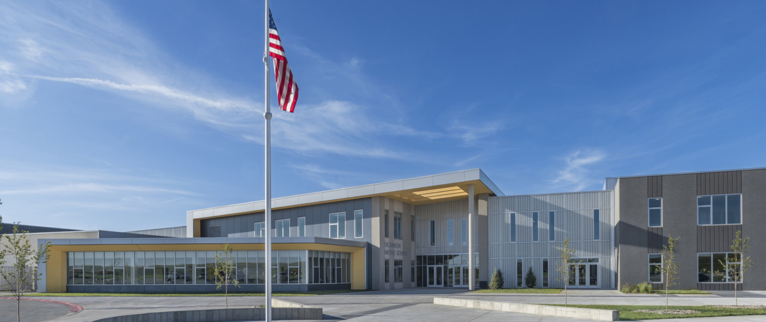 Exterior of 2 story grey panel building with silver wrapped facade and yellow under side of overhangs and canopy. Flag, front