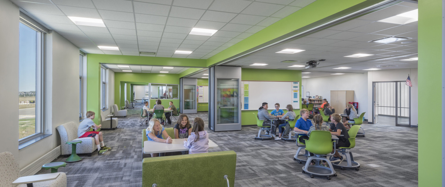 Large white room with green accents and flexible seating. Flexible interior walls create smaller spaces. Windows, left