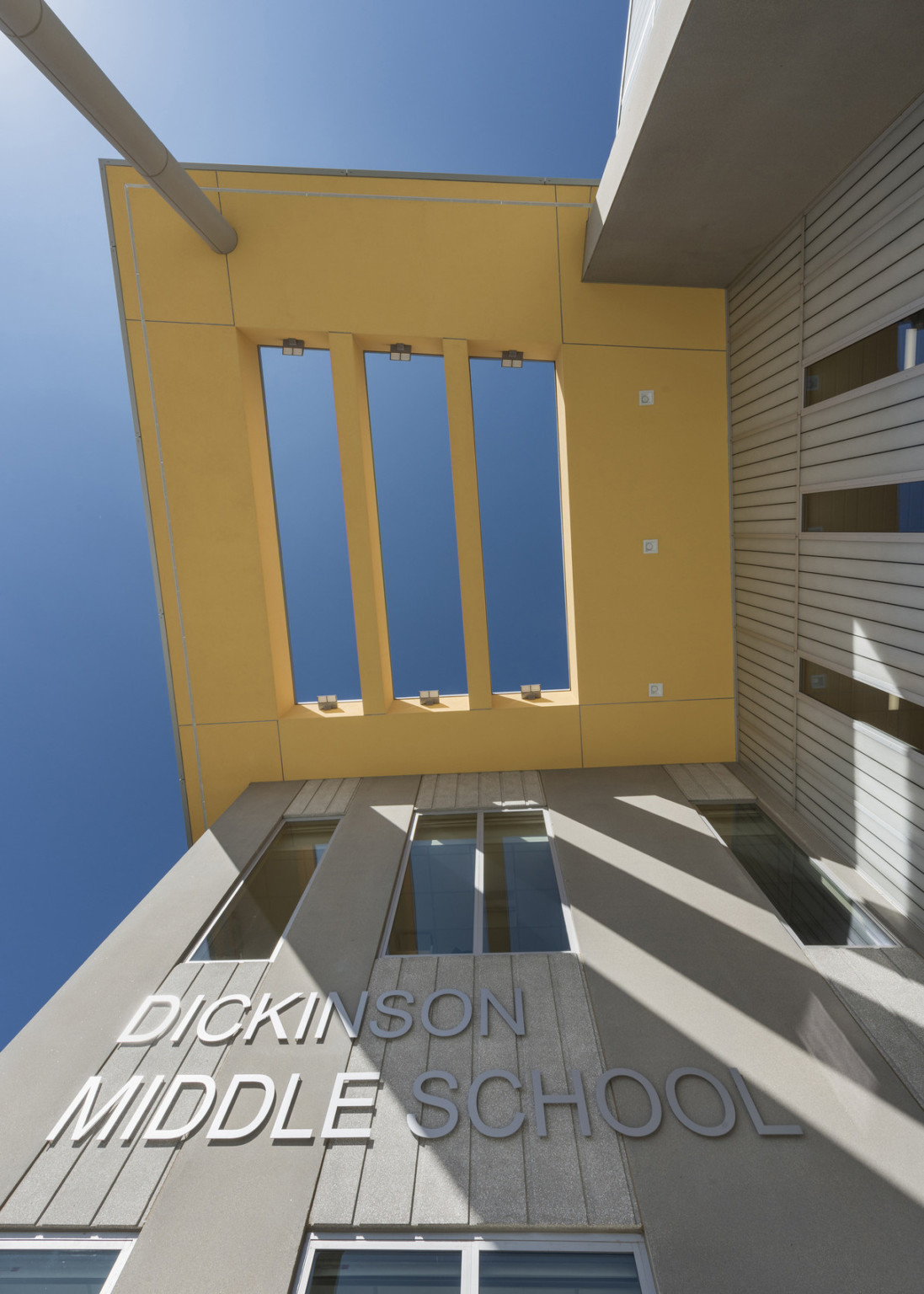 Looking up to canopy over entrance with 3 rectangular skylight cutouts over grey panel wall with Dickinson Middle School sign