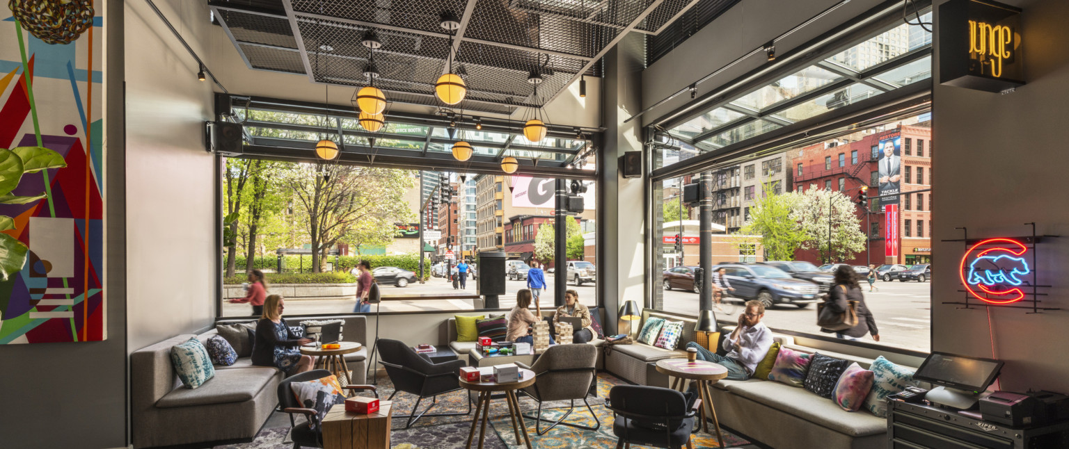 Interior corner with flexible and comfortable seating, windows on both walls opened. Geometric metal pendant lights hang