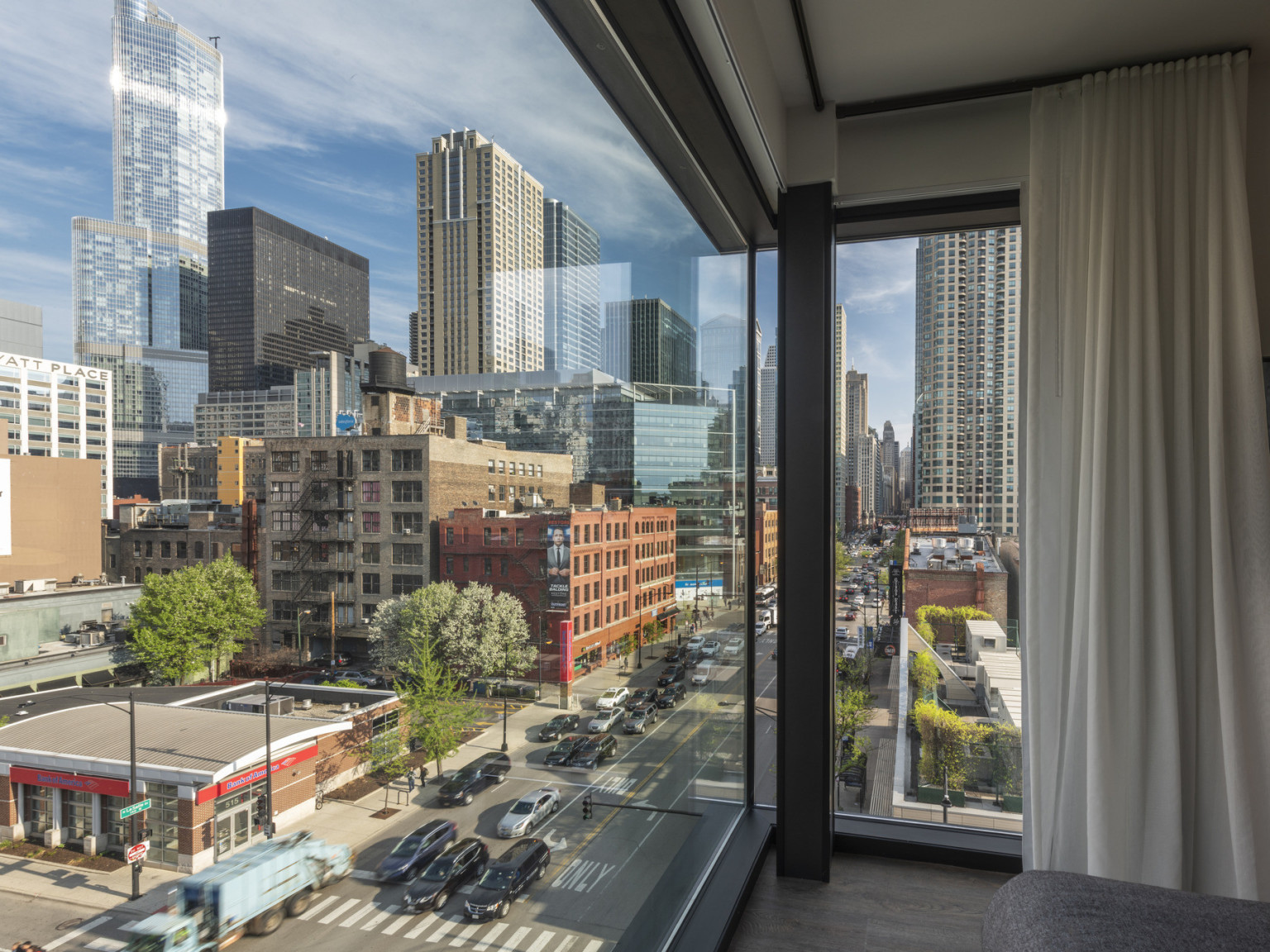 Guest room with floor to ceiling windows wrapping around corner of room with thin dark column and white curtain