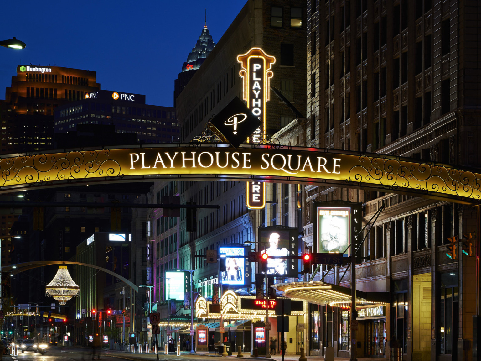 Sign reading Playhouse Square illuminated at night with scroll detailing on both sides in front of block of tall buildings