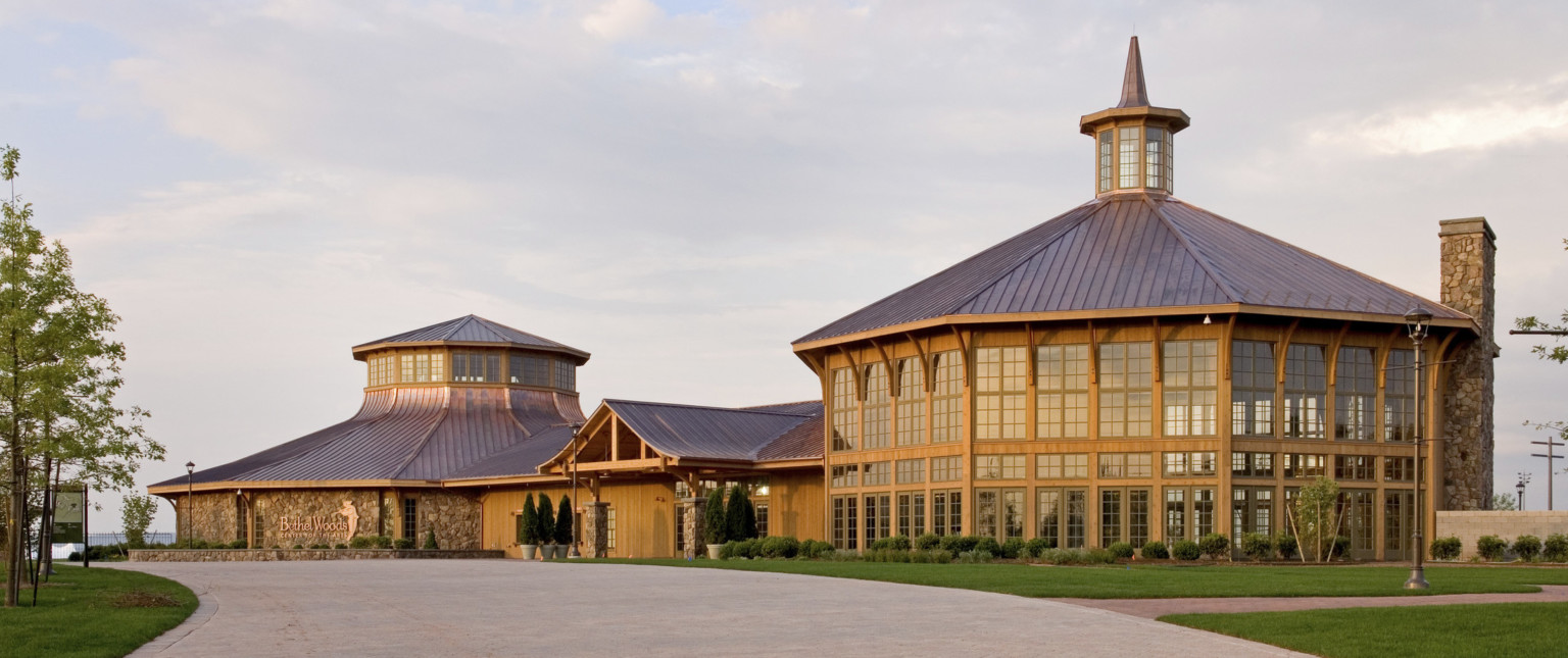 Rounded wood and window building with central spired cupola is connected by a single story entry to a round stone building