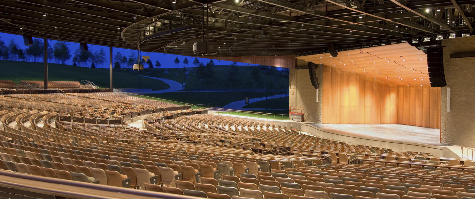 Light brown seats under black amphitheater roof facing wood paneled stage with rounded panel ceiling and recessed lights, amphitheater design, open air amphitheater; Bethel Woods Center for the Arts