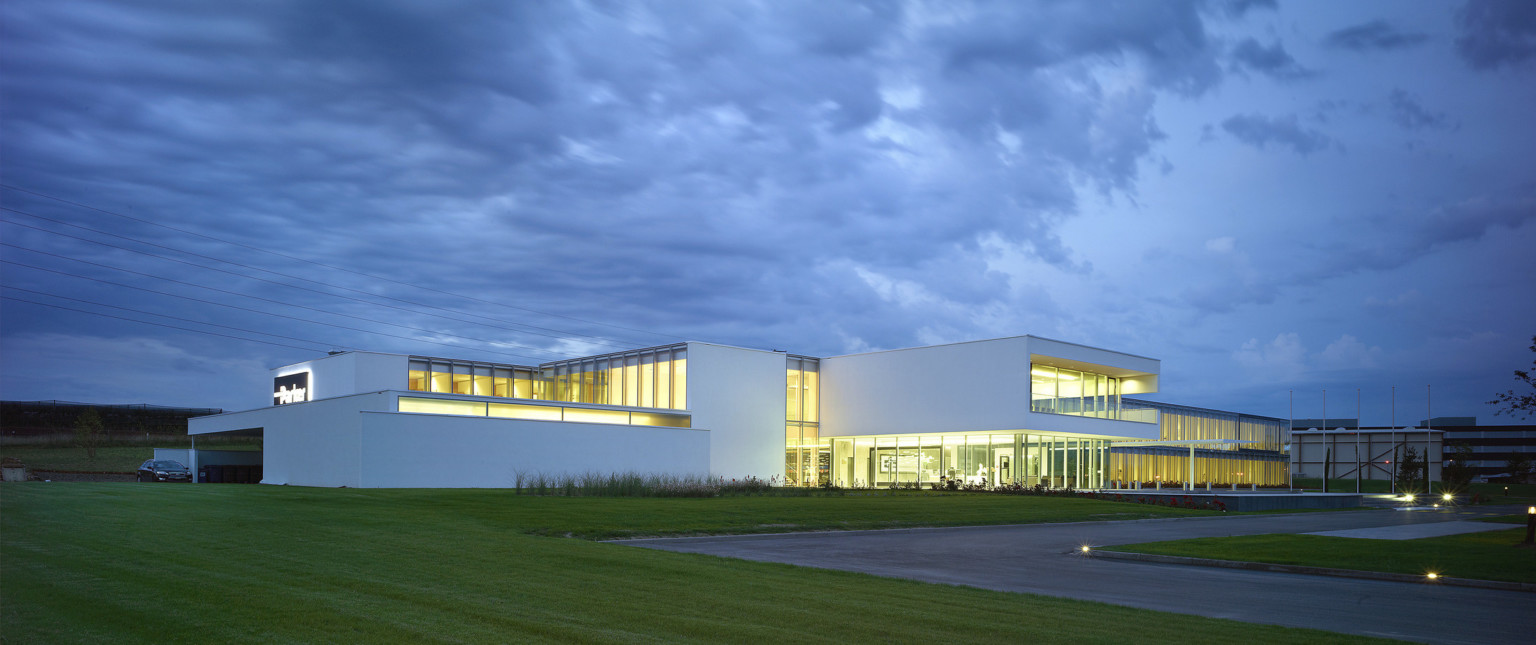 Corner view from across lawn of 2 story building with white wrapped facade around large sections of floor to ceiling windows