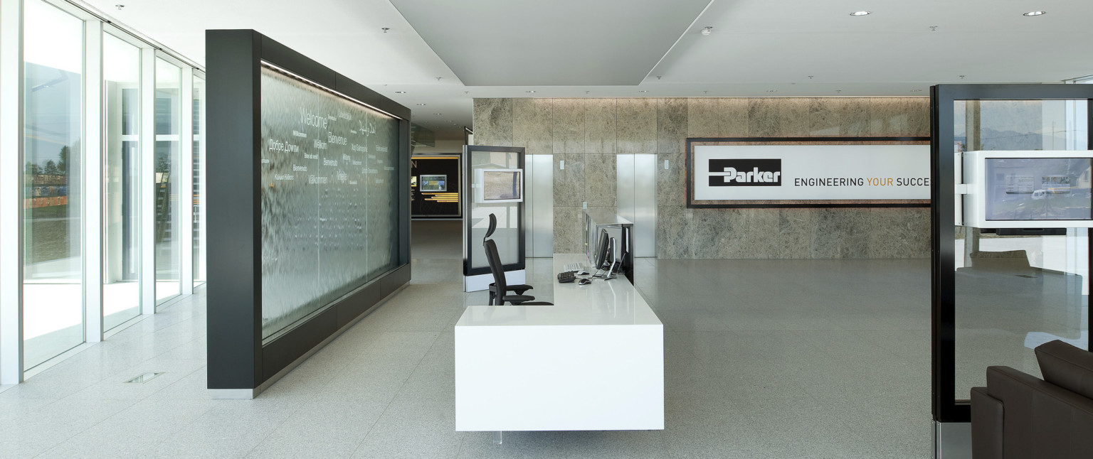 White reception desk in front of black framed translucent wall with different languages. Across, stone wall with Parker logo