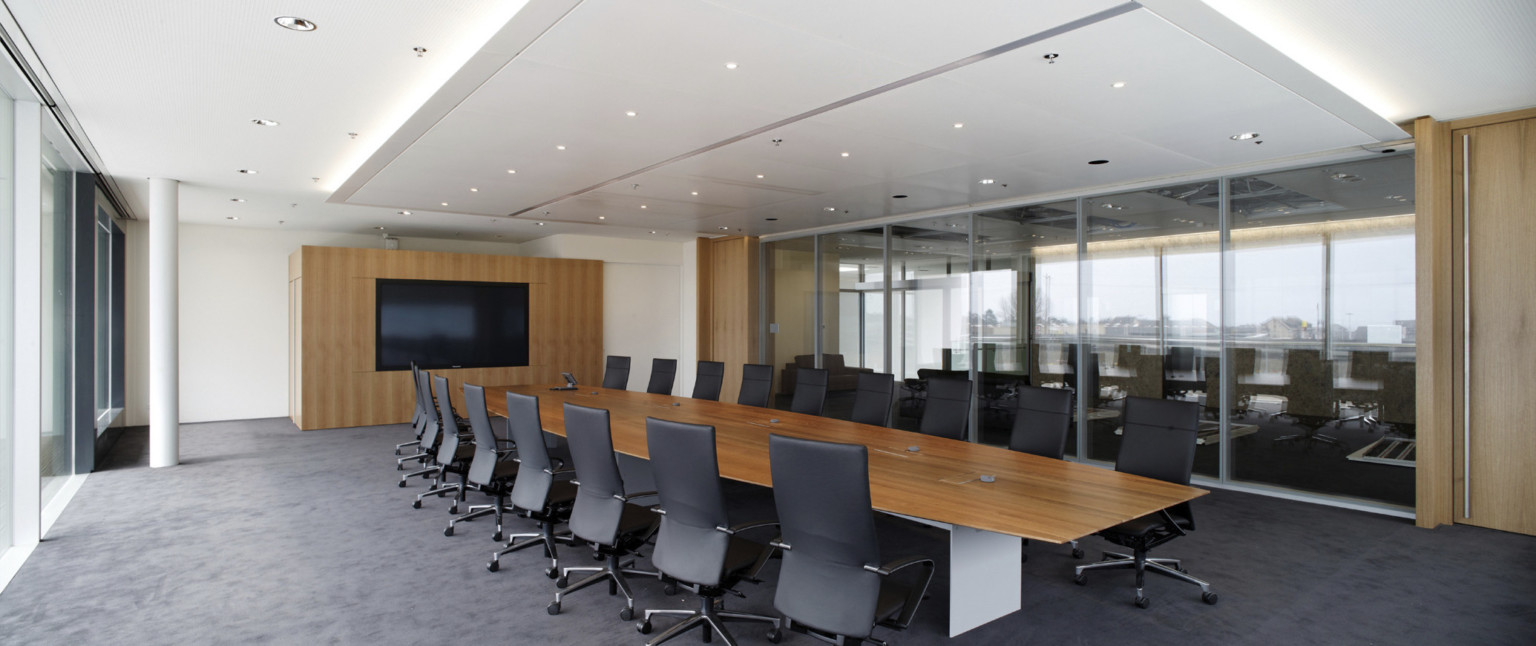 Conference room with long wood table and chairs across from wood accent wall with screen. Interior floor to ceiling windows