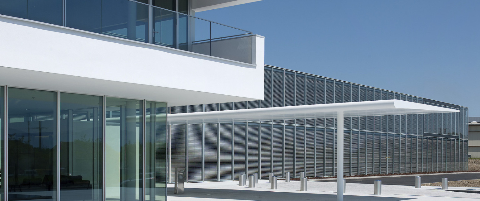 Front entrance with white canopy behind floor to ceiling windows under white 2nd floor balcony with glass rail