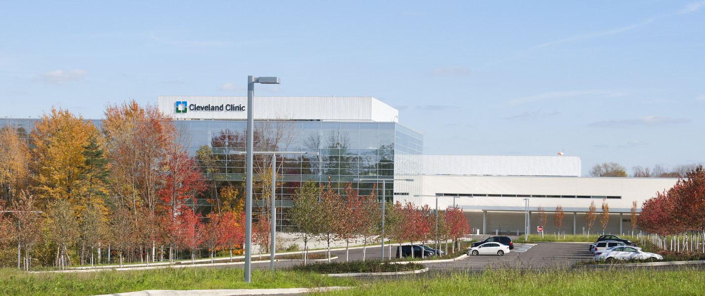 View of white and glass building from grass across the parking lot. Sign over glass building section reads Cleveland Clinic