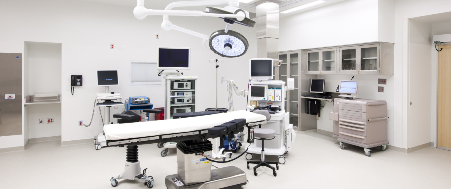 Operating room with bed center, movable lights hang from above. Stool at head next to portable screens and equipment