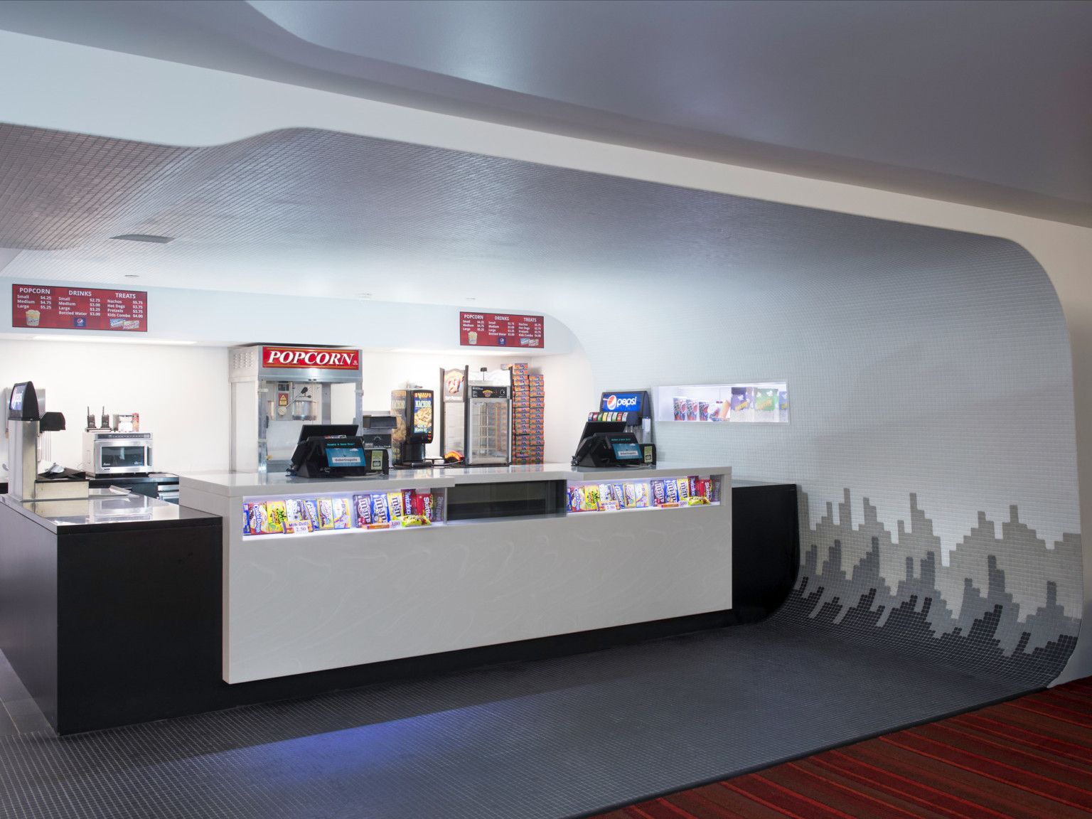 Concession stand sits in curved pocket of room with gradient tiled pattern flowing from black floor up the wall to white