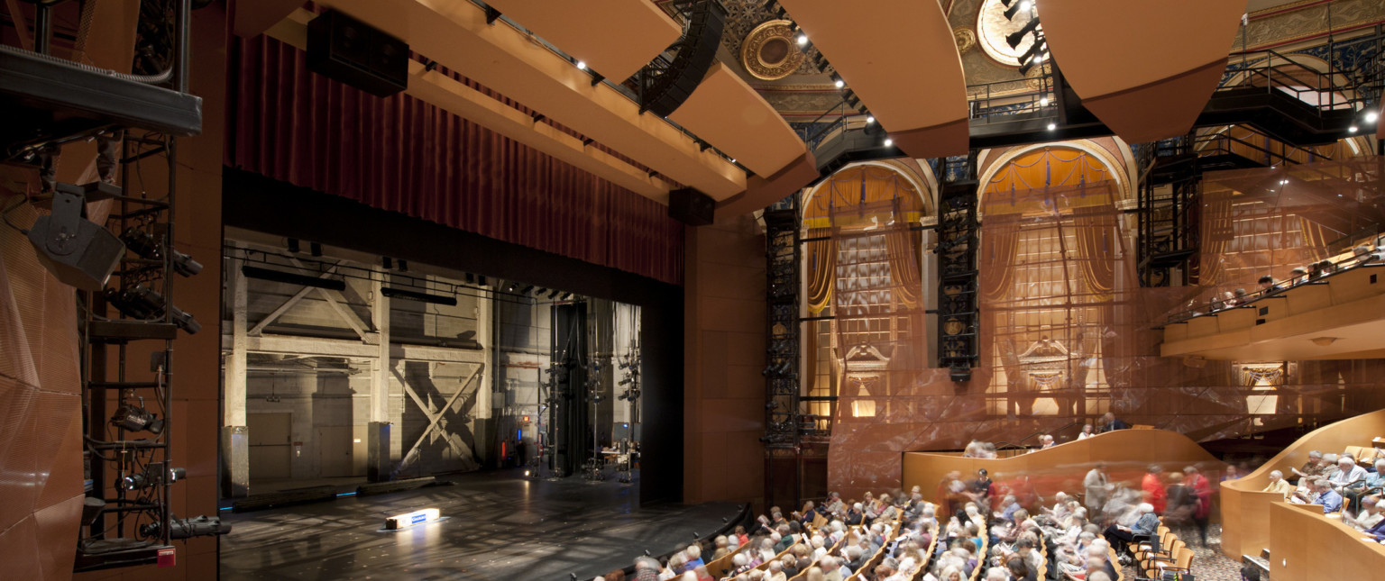 Theater seen from the side over the audience with large arch shaped windows. The stage is empty and stage right can be seen