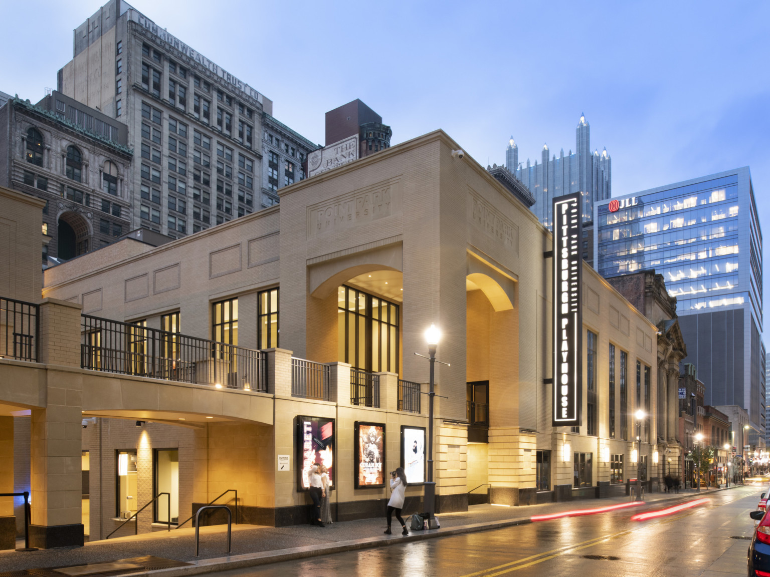 Exterior view of tan building with black illuminated Pittsburgh Playhouse sign, below ground entry and second floor walkway