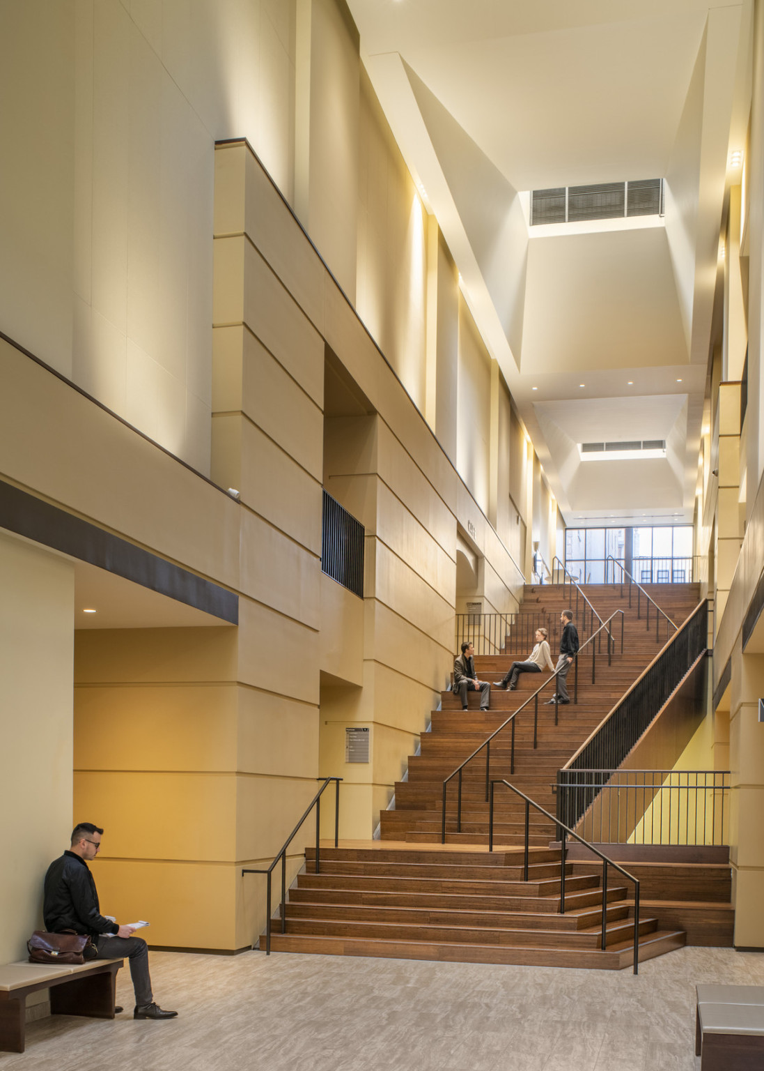 People sit in wide section of wooden stairwell between geometric wall details