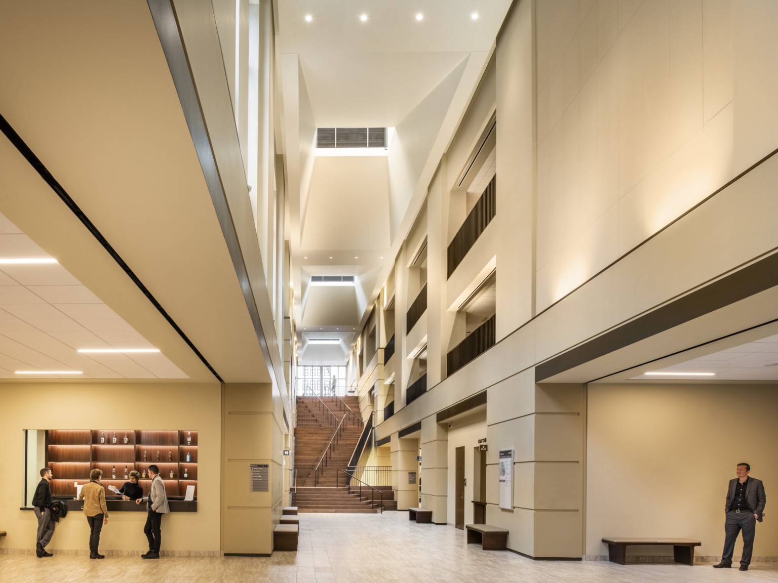 Hallway leading to diagonal wooden staircase, angled cutouts beginning at second story of ceiling to rectangular skylights