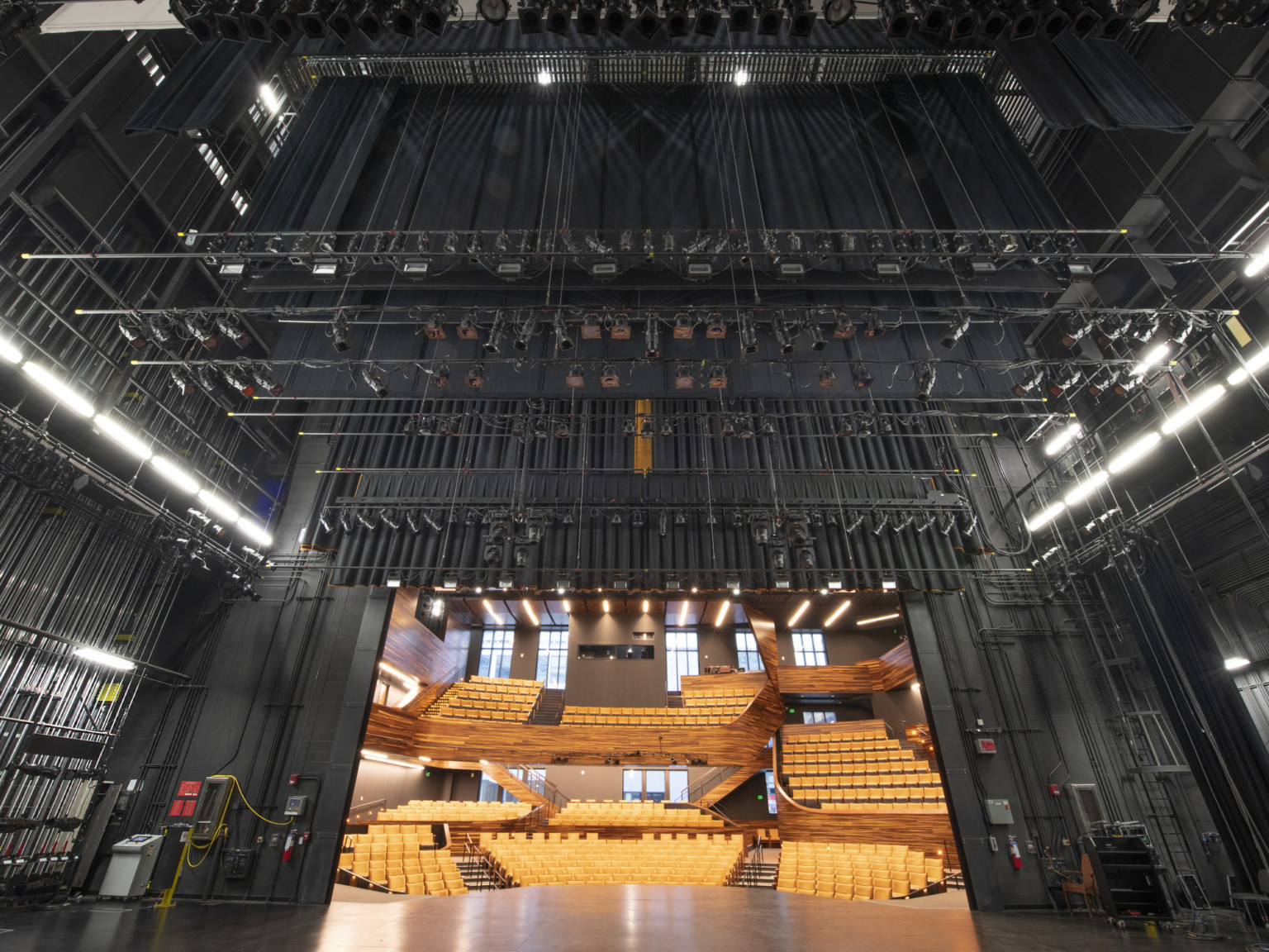 Looking from backstage outwards to dark colored stage rigging system hidden from yellow empty audience seats