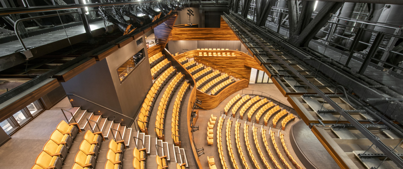 View from above the balcony looking down, there are catwalks above the seating and in the balcony is a grey room with window