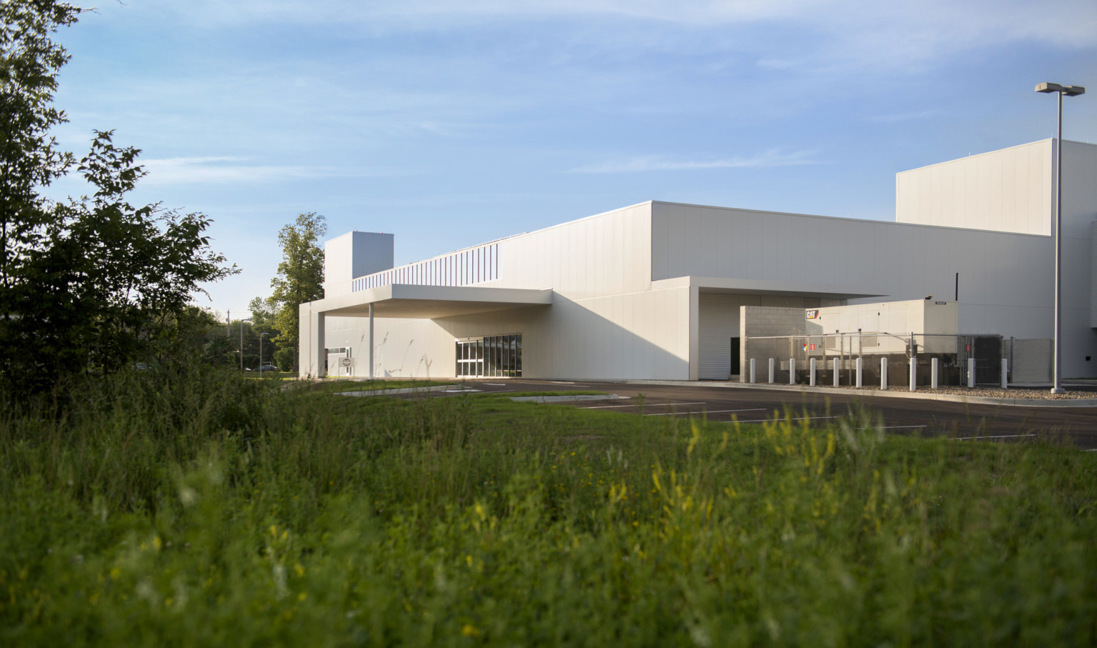 grass and trees in foreground of white modern angular building side entrance with sliding glass doors covered by white canopy