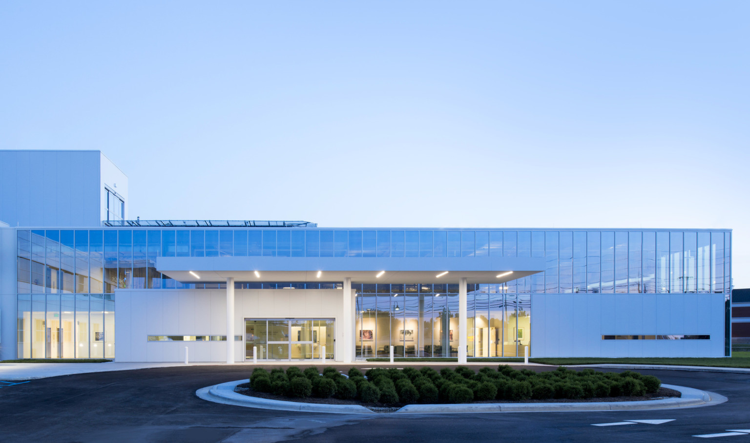 white modern building with large windows and awning illuminated by strips of light against a dusk sky