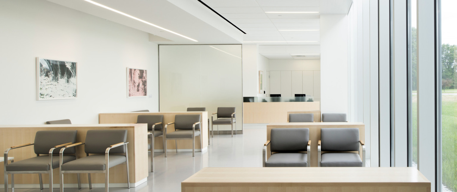 White room with seating area separated from wood reception desk by translucent glass. Wood dividers between seating sections