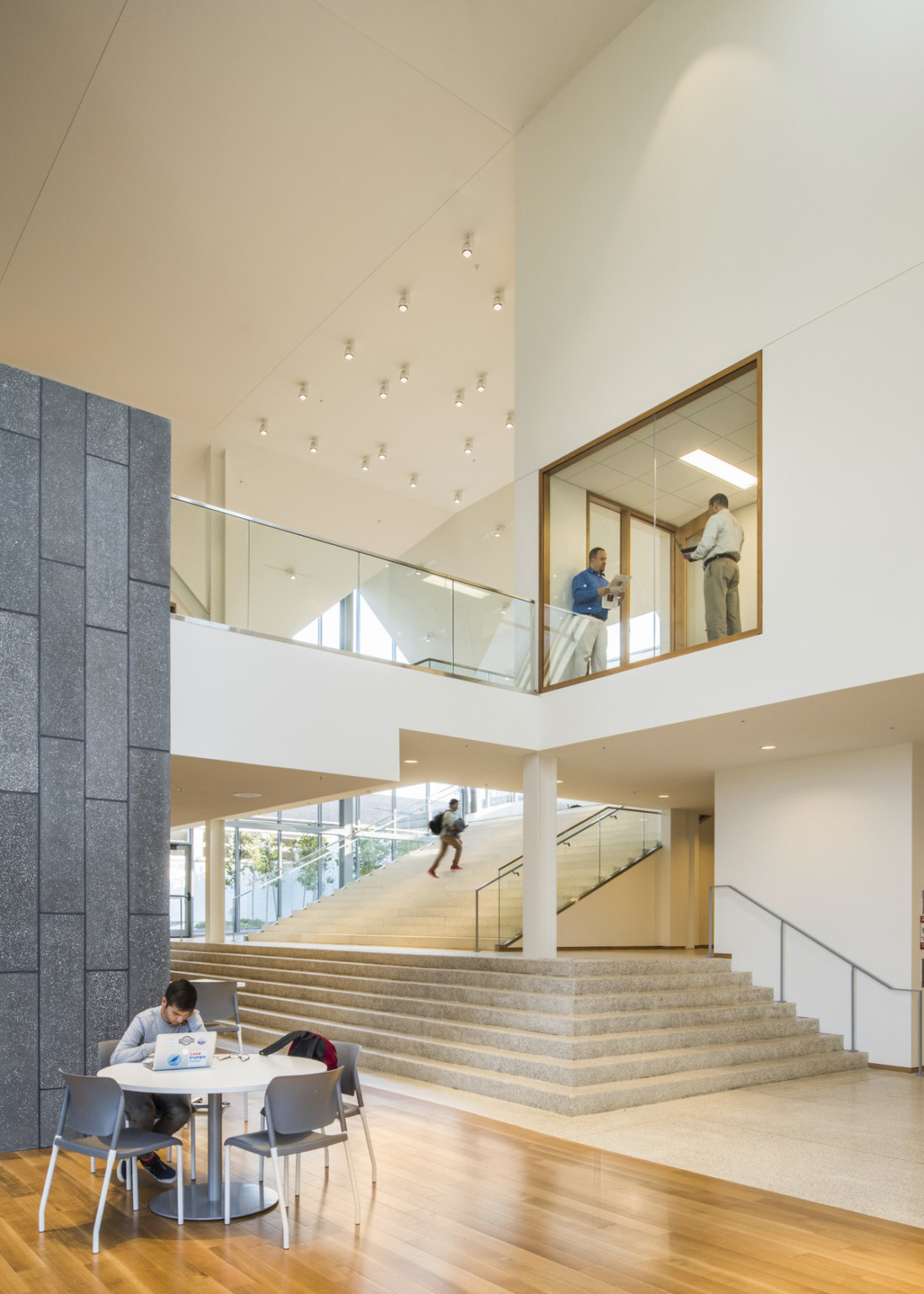 Wood floor atrium with table in front of a stone accent wall. Behind, a white hall with stairs and exposed 2nd floor walkway