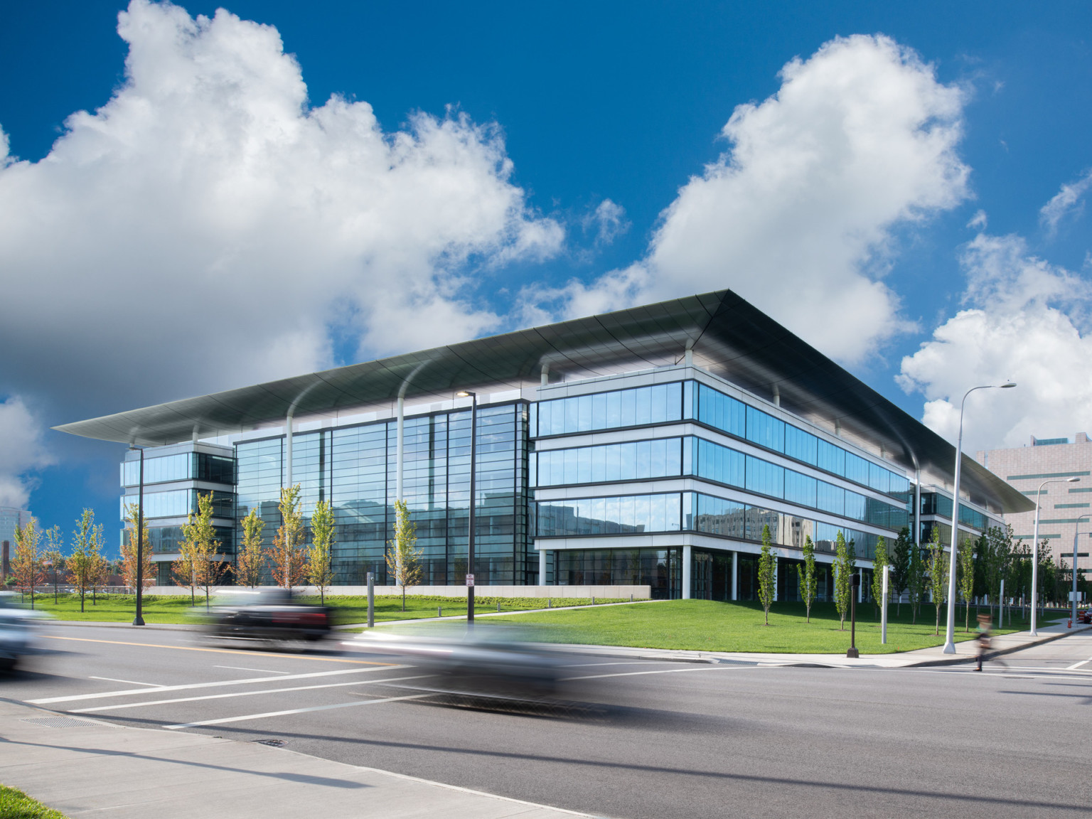 Building with 4 stories of floor to ceiling windows and recessed window wall center, with grey metallic overhang covering all