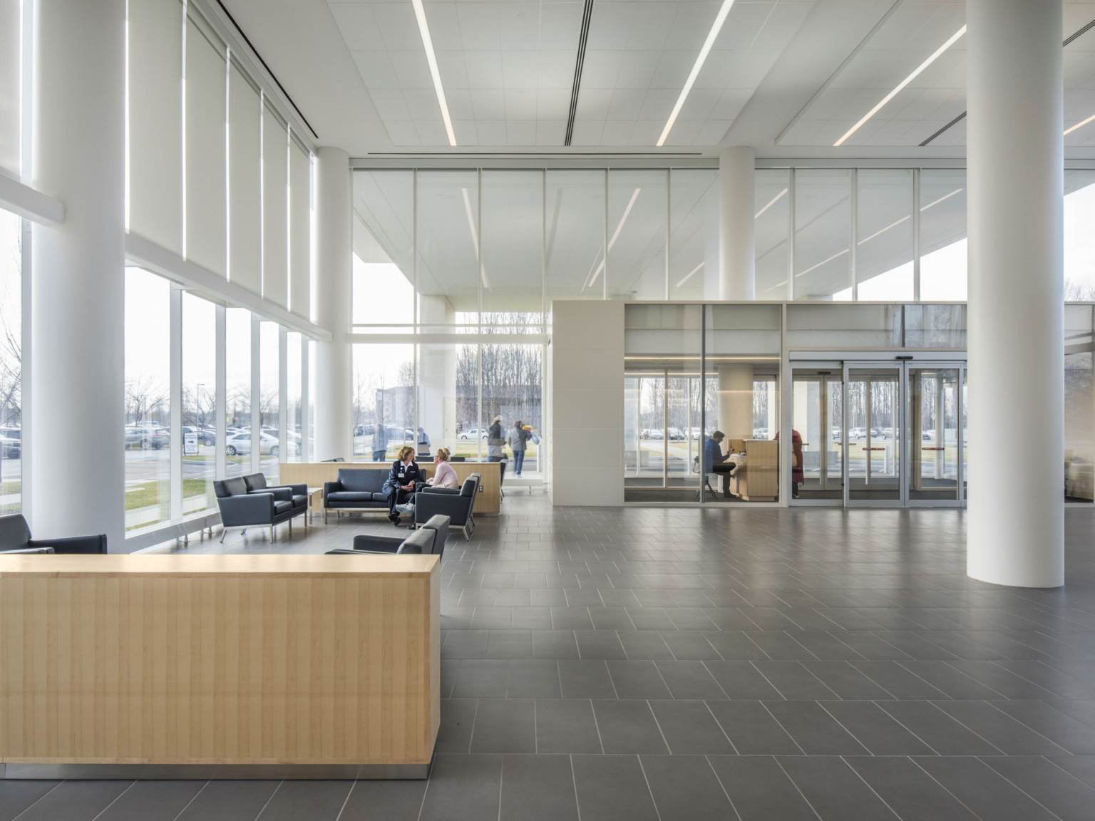 Lobby with double height windows and glass antechamber. Seating area is to the left with couches in a white room with pillars