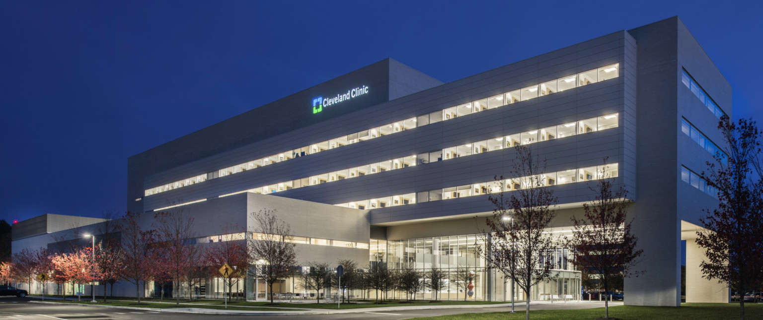 Hospital illuminated at night, seen from across the street facing drive up glass doors. Entry area has double height windows