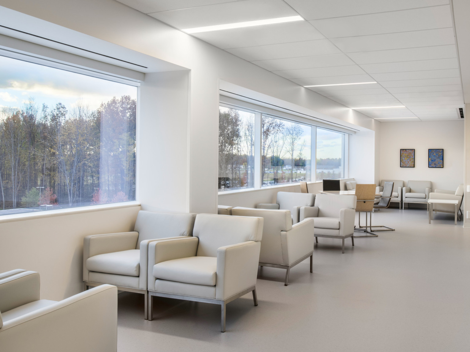 Seating area with beige armchairs along wide windows in a white room