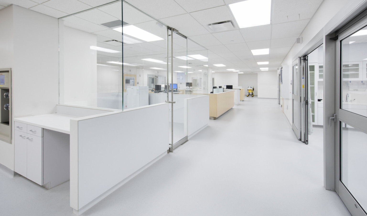 Bright white emergency room nurses stations opposite patient rooms have glass walls for visibility