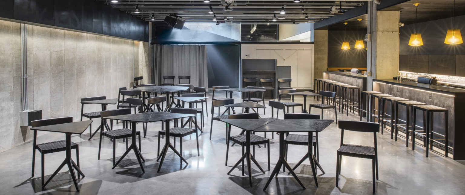 Seating area with triangular tables that can combine for multiple people, next to bar at right with stools