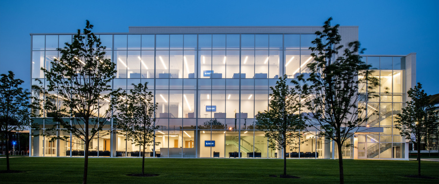 Side of building at night, illuminated so all 3 floors are visible through the floor to ceiling windows