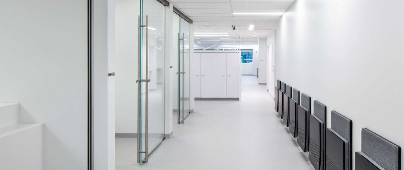 Hallway with glass sliding doors to the left and folded seats along right wall. White cabinets stand at the end of the hall