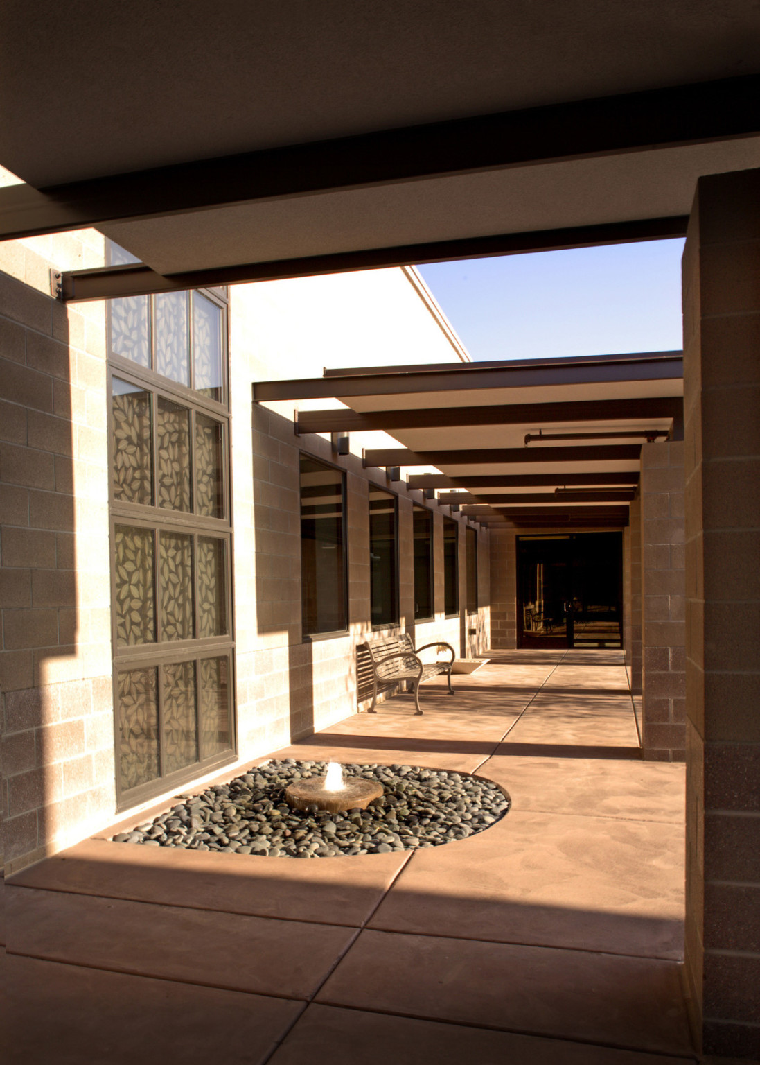 Walkway along side of building partially covered by sections of awning with support beams between wall and stone pillar