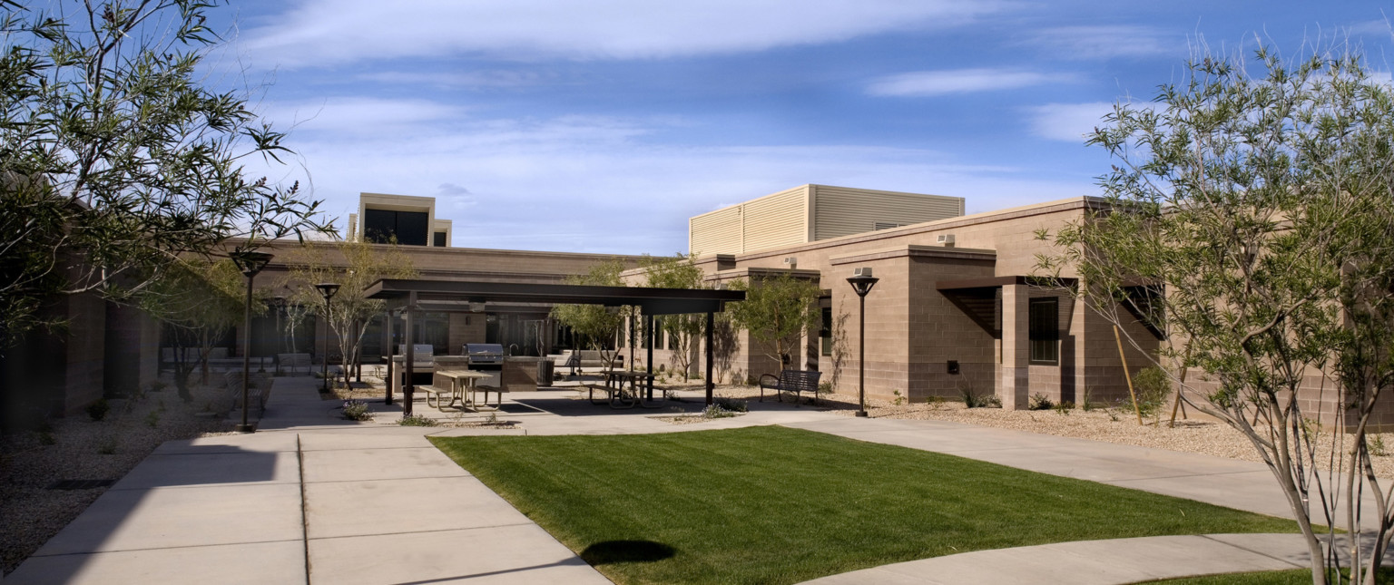 Grass section in courtyard in front of picnic tables under large shelter with 2 grills built into stone counter with sink