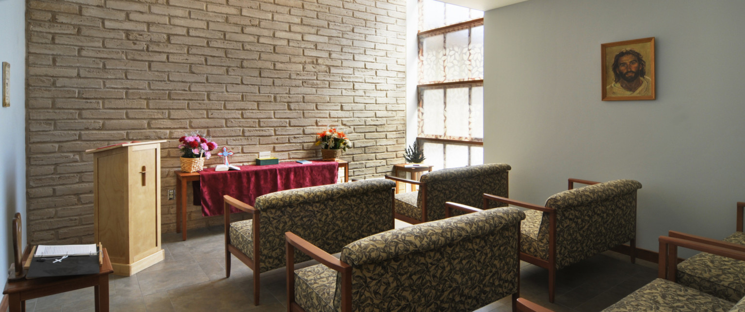 Small chapel with large comfortable chairs facing exposed brick wall with podium and table. Translucent glass window right