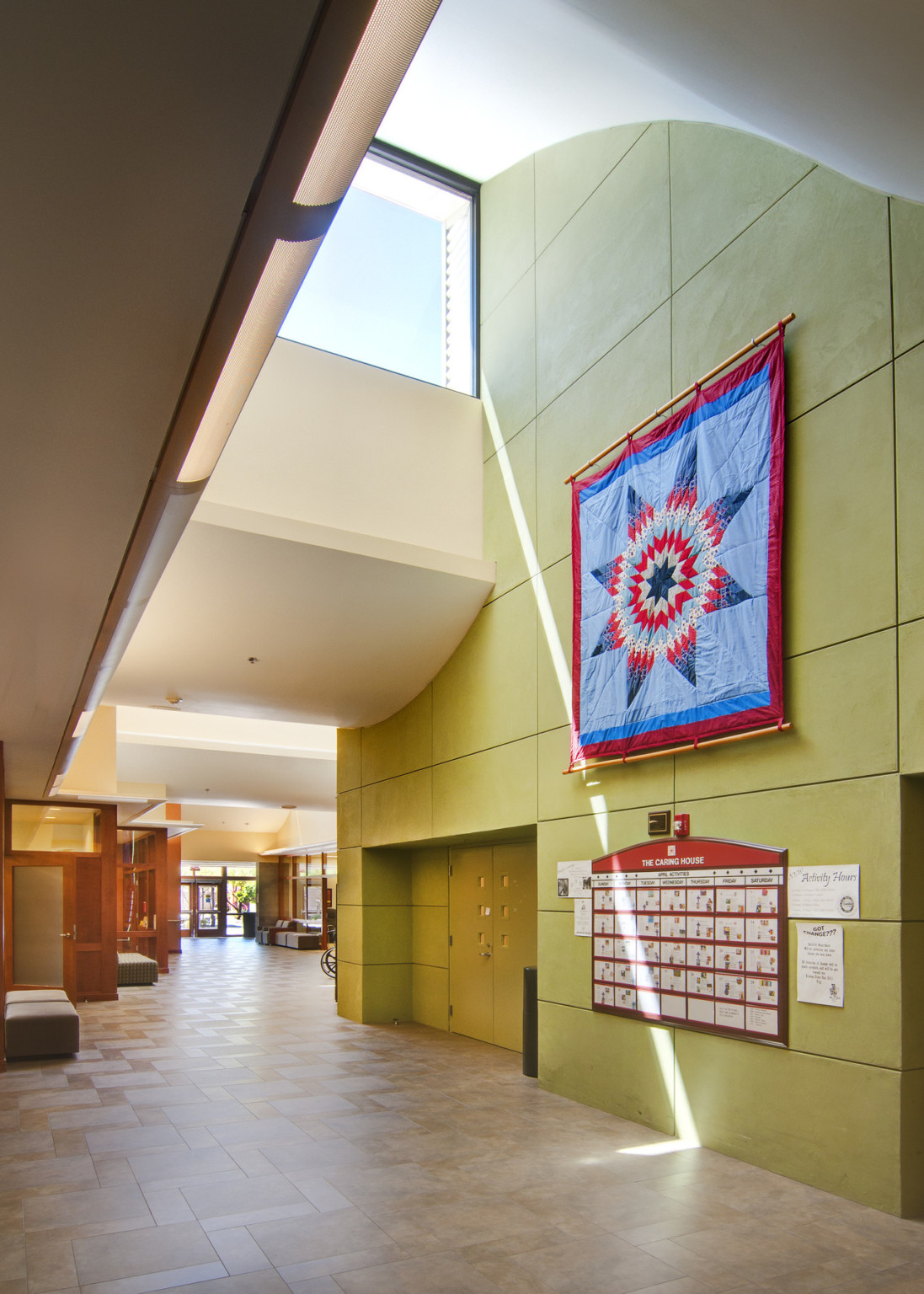 Green wall, right, in hallway under dramatically curving white ceiling with square window. Geometric tapestry hangs on wall