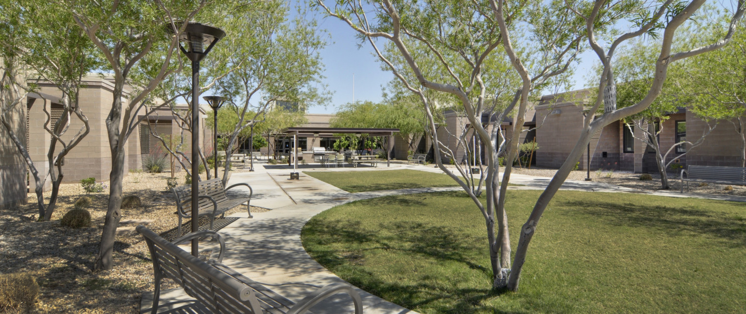 Rendering of courtyard with trees in a mixture of grass and gravel surrounded by stone building. Covered seating area to back