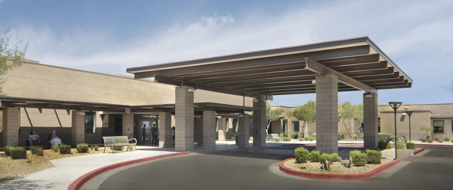 Covered front entry to building with grey overhang below shelter over driveway, both supported by stone pillars