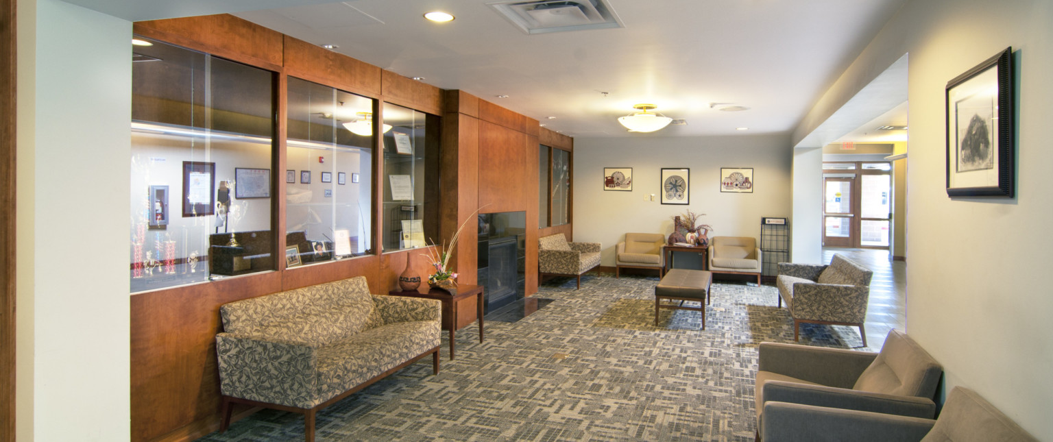 Carpeted interior seating area off hallway with couches and chairs, a black fireplace built into wood wall with glass shelves