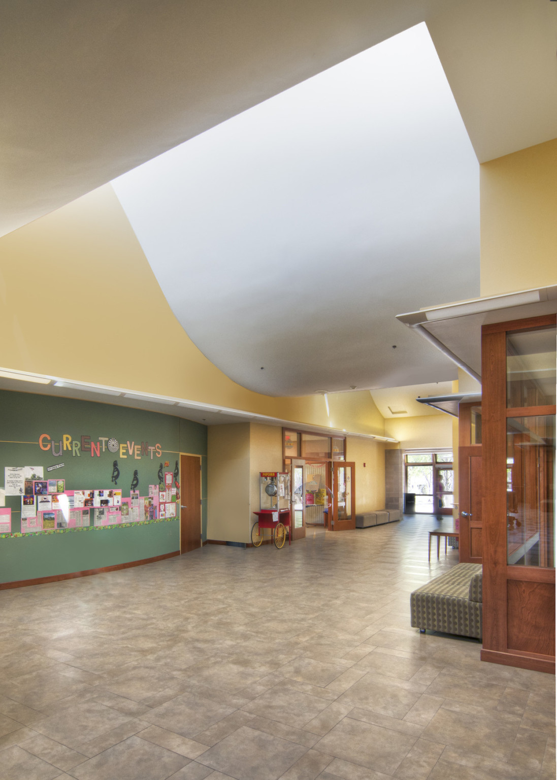 Yellow double height hallway with green lower accent wall below curving white drop ceiling. Wood shelves and door right