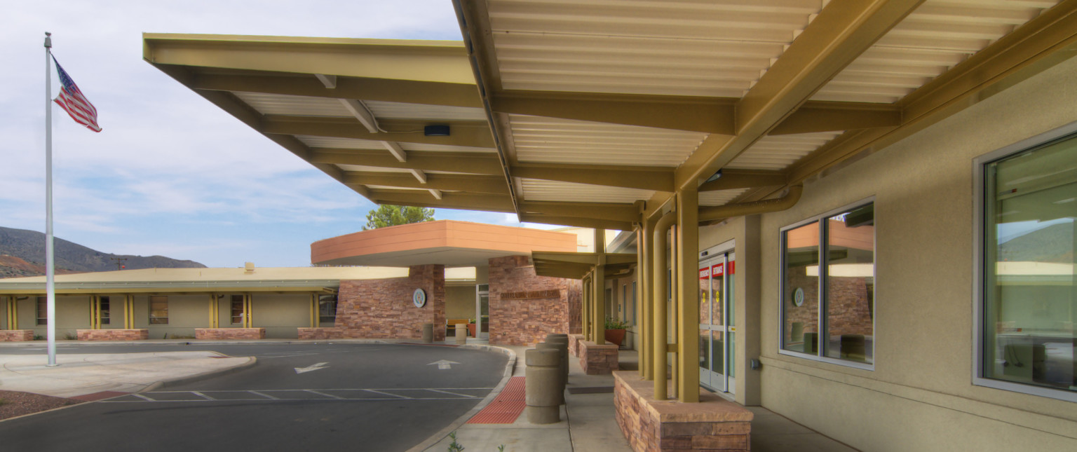 Rendering of front of building near emergency room entry. White textured overhang seen from beneath with yellow pillars